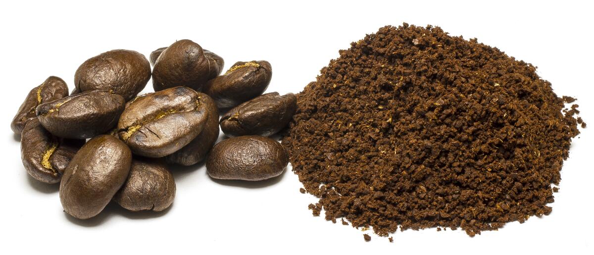 Coffee beans with a pile of coffee dust on a white background