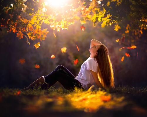 A young brown-haired girl in the autumn forest basking in the sunlight