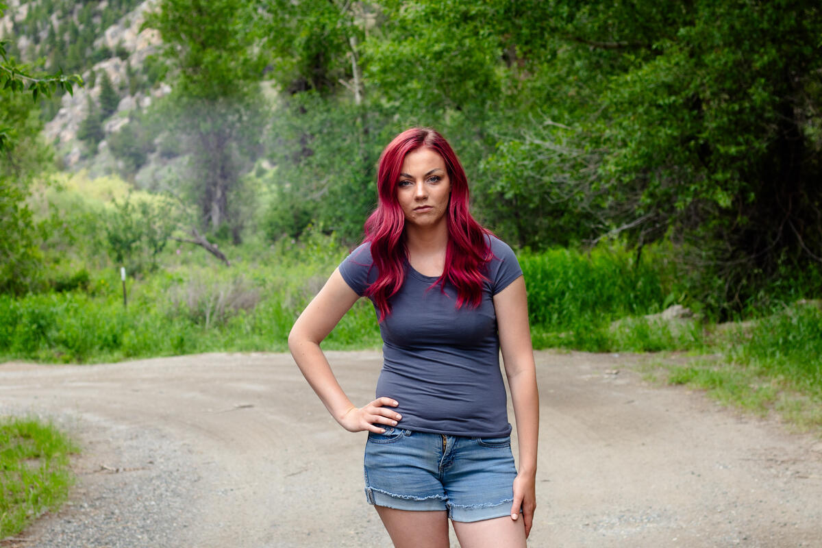 A girl with pink hair stands on a forest road