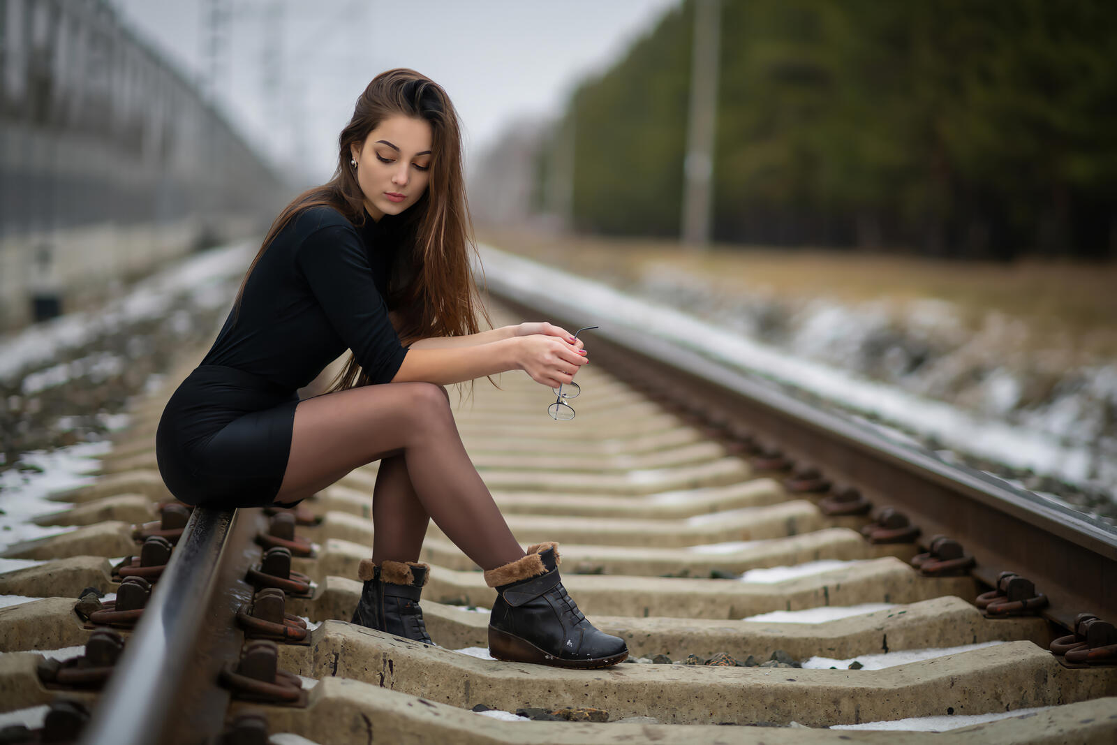 Бесплатное фото Девушка в черном платье сидит на железной дороге