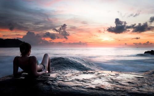 Девушка с красивой фигурой лежит на камне у моря