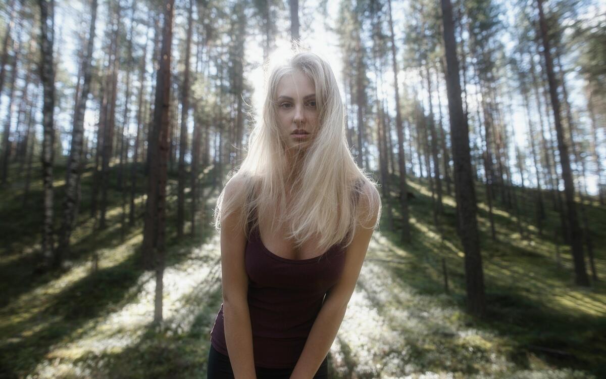 Белобрысая девушка в хвойном лесу в солнечную погоду