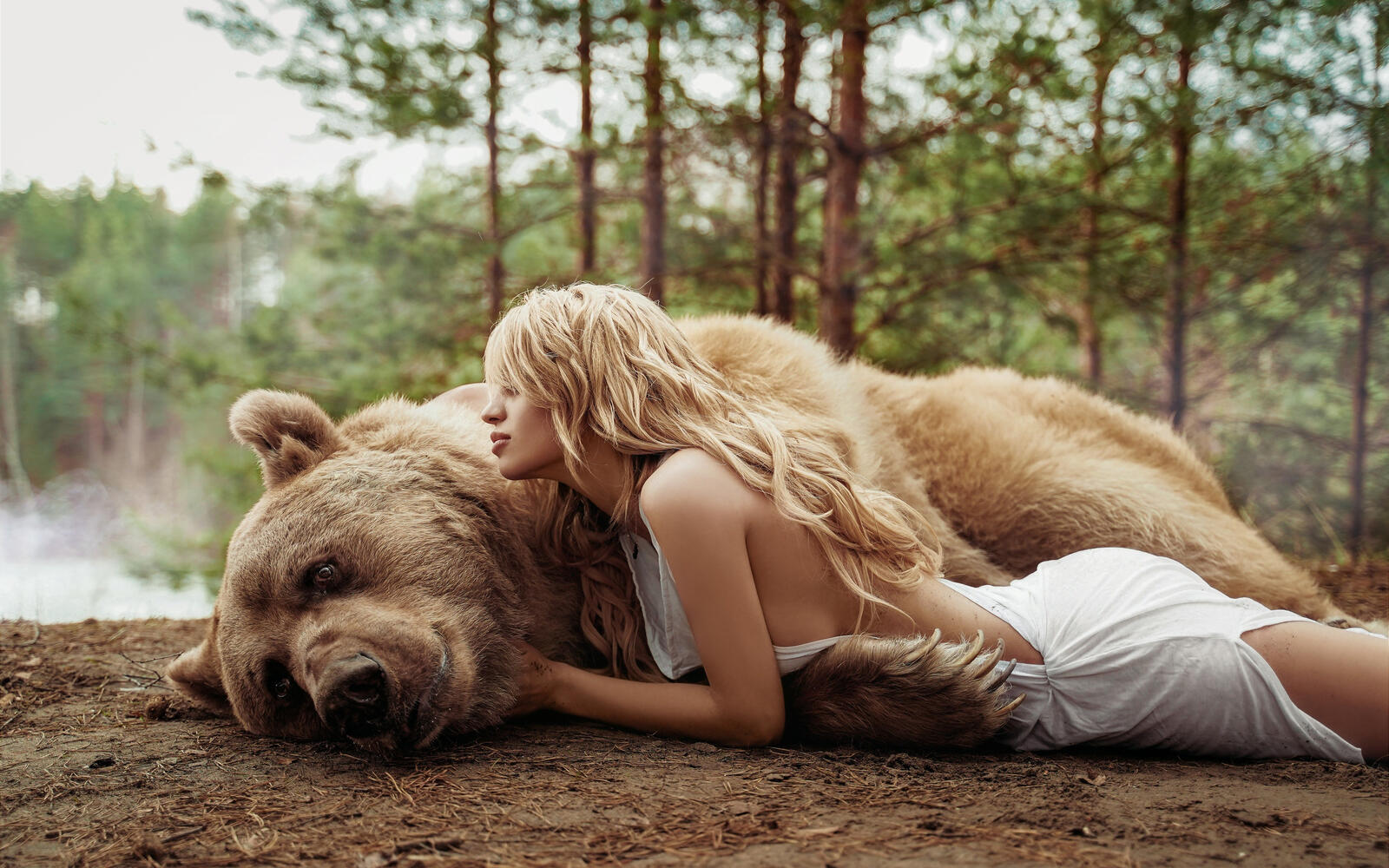 Free photo A girl lying with a bear on the shore of a lake