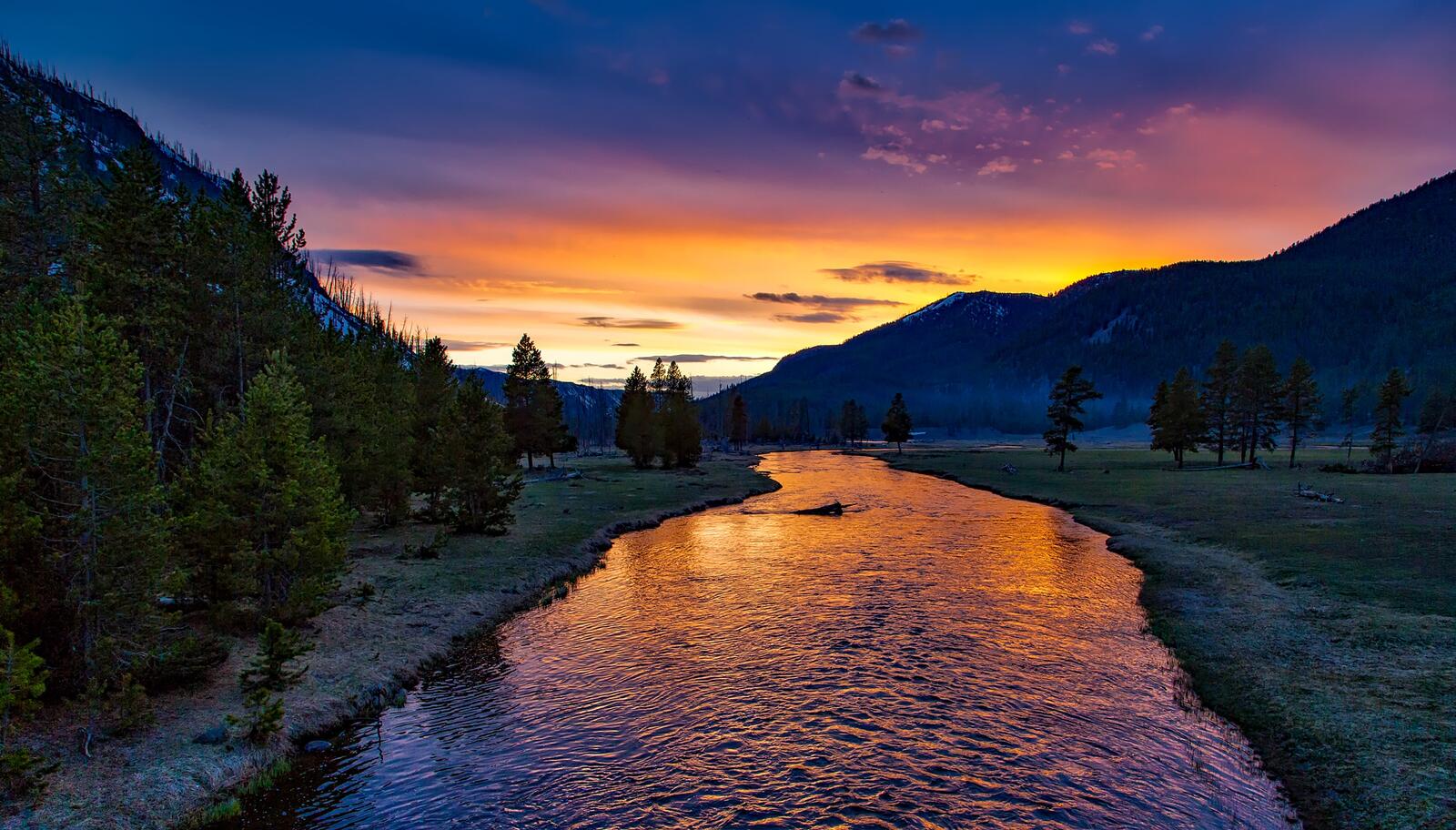 Бесплатное фото Спокойная река протекает вдоль красивой лужайки на закате