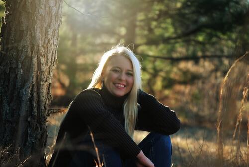 Dyed blonde in black sweater smiles sitting by the tree