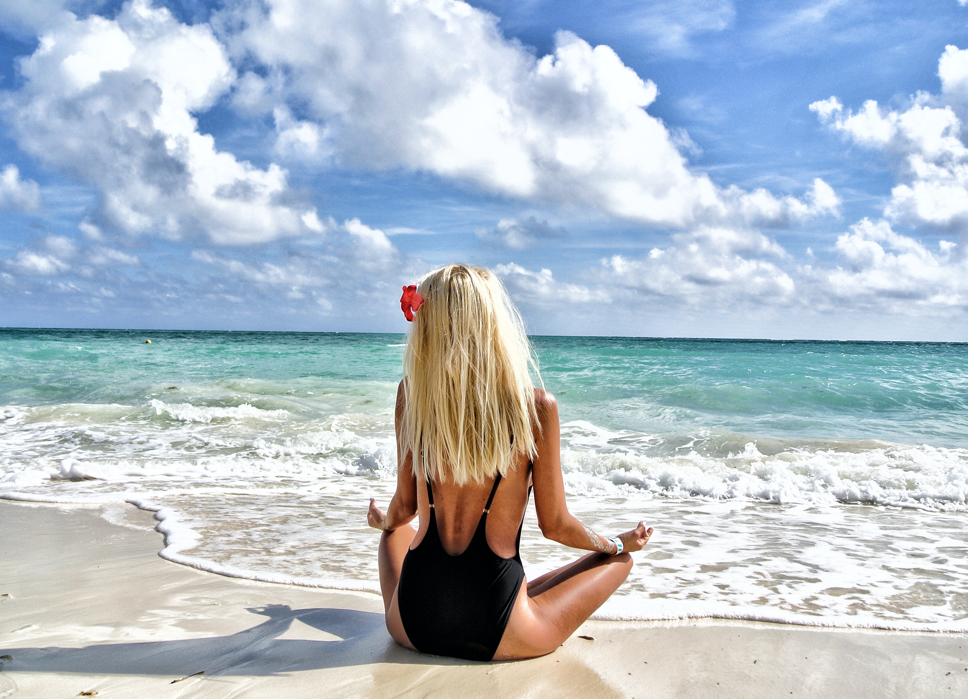 A blonde meditates on the beach.