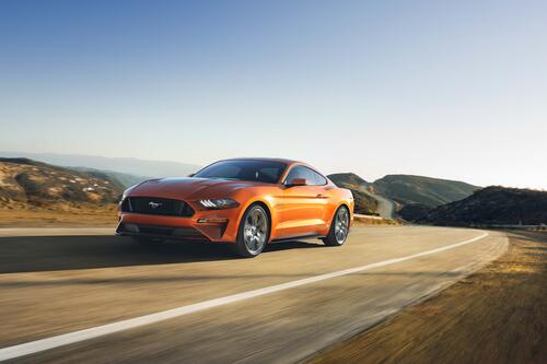 An orange Ford Mustang drives down a country road
