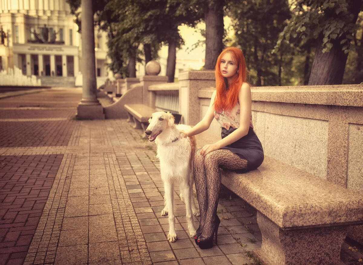 Рыжеволосая девушка сидит на скамейке с собакой