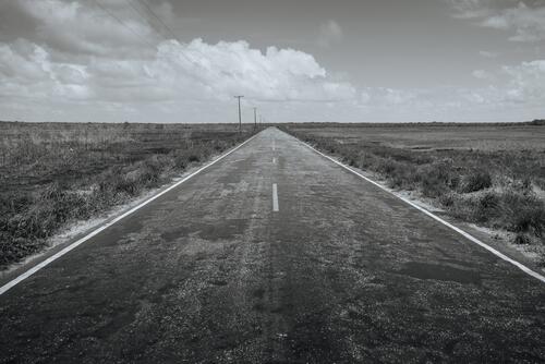 Black and white landscape with an asphalt road going into the horizon