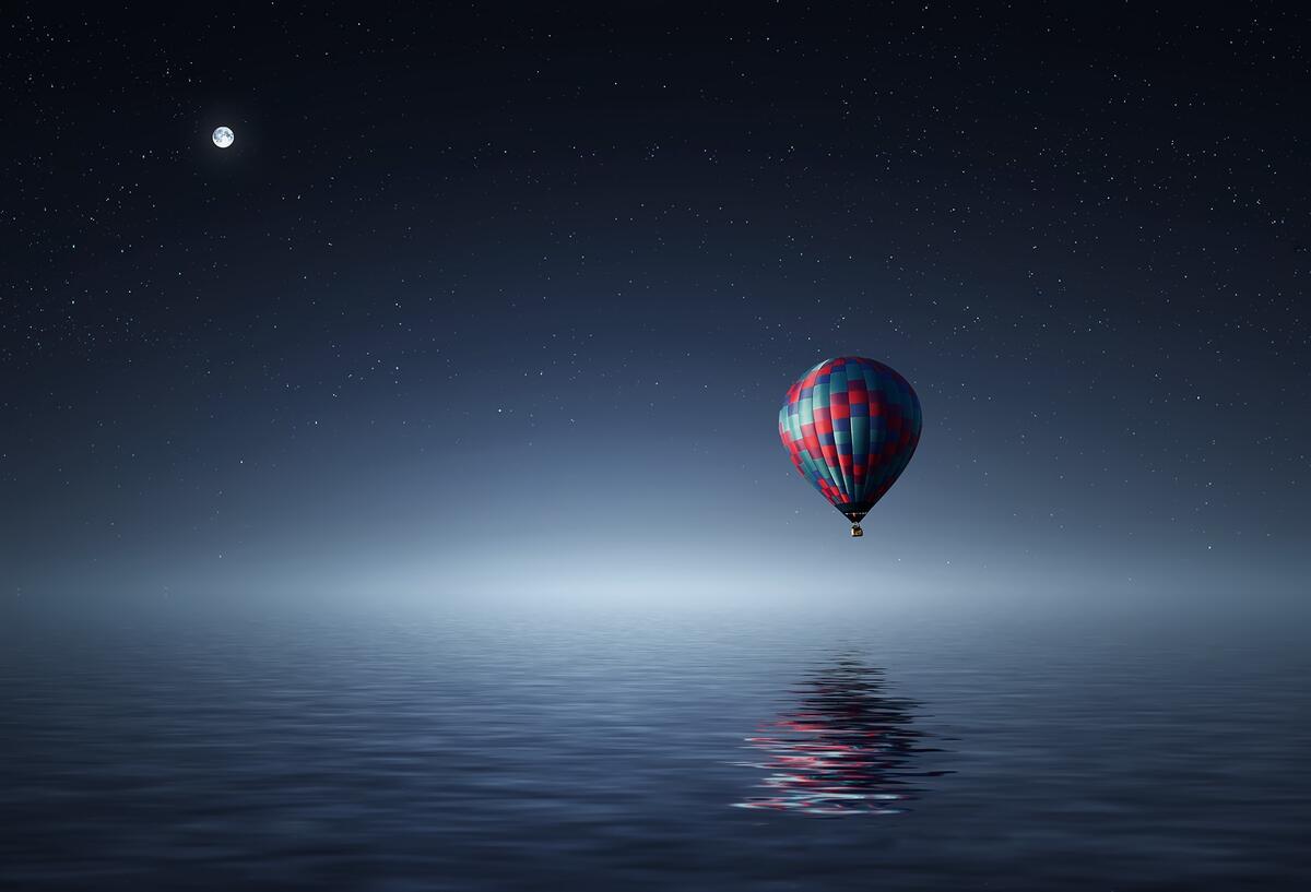 A lone balloon flies over the ocean at night.
