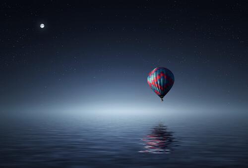A lone balloon flies over the ocean at night.