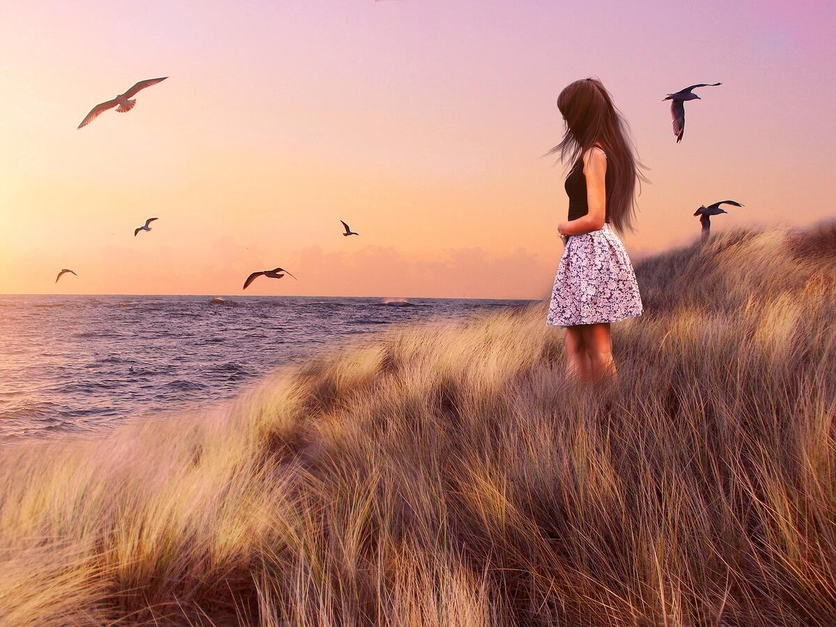 A girl in a dress standing near the shore where the seagulls fly