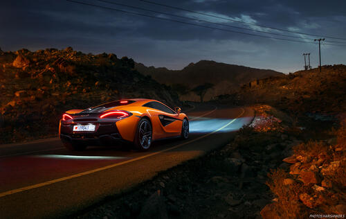 A picture of an orange Mclaren on a country road.
