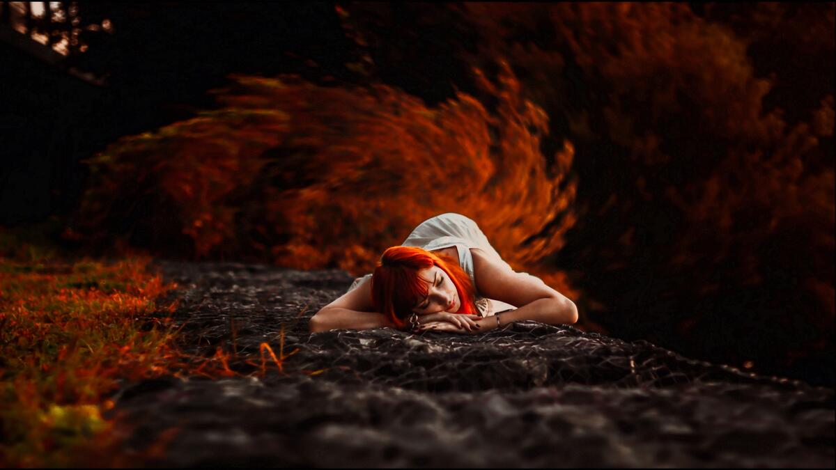Redheaded girl lying on the ground against the background of autumn grass