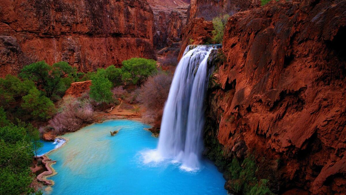 Picture of a waterfall off a cliff into blue water in a canyon