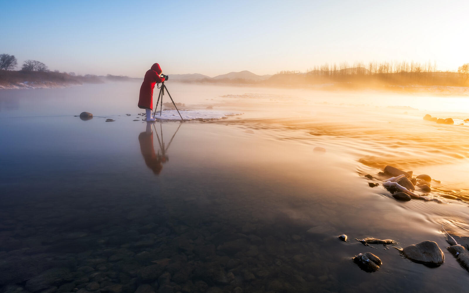 Free photo A photographer takes stunning sunrise shots on a shallow river