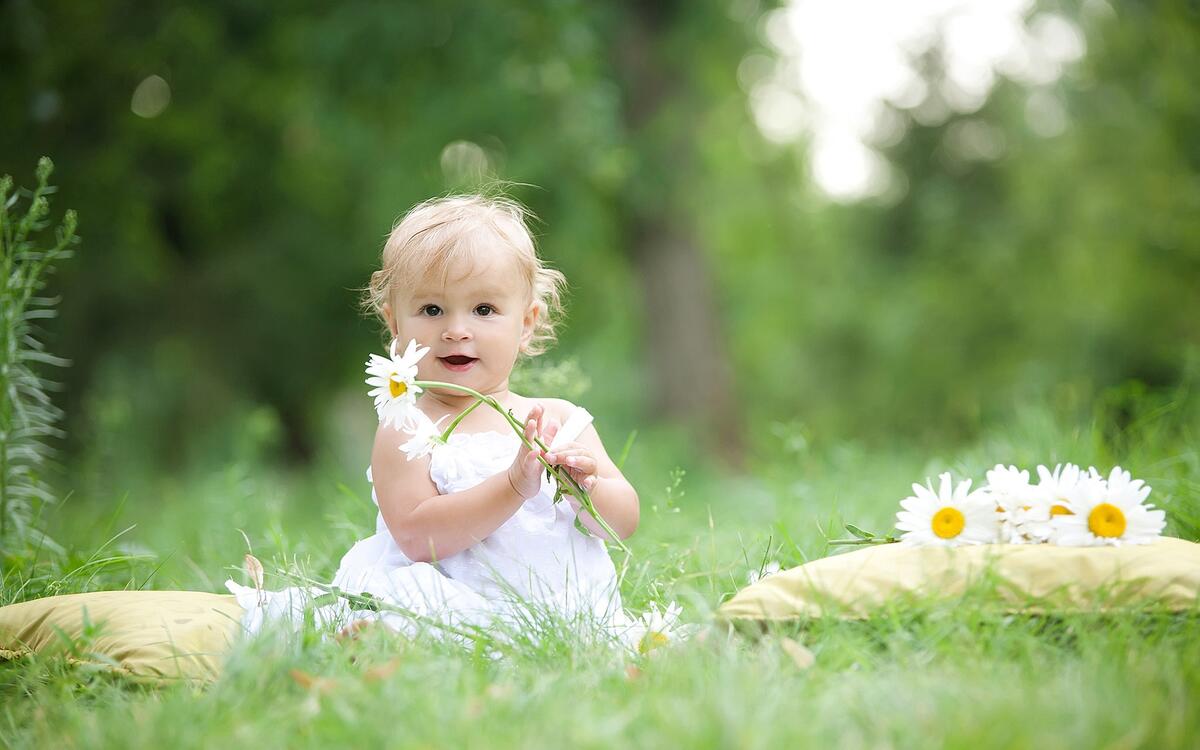 A little girl in a white dress sits in a green meadow