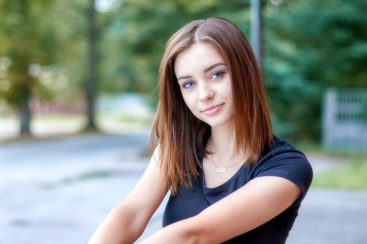 Beautiful brown-haired girl with blue eyes smiling on a park bench