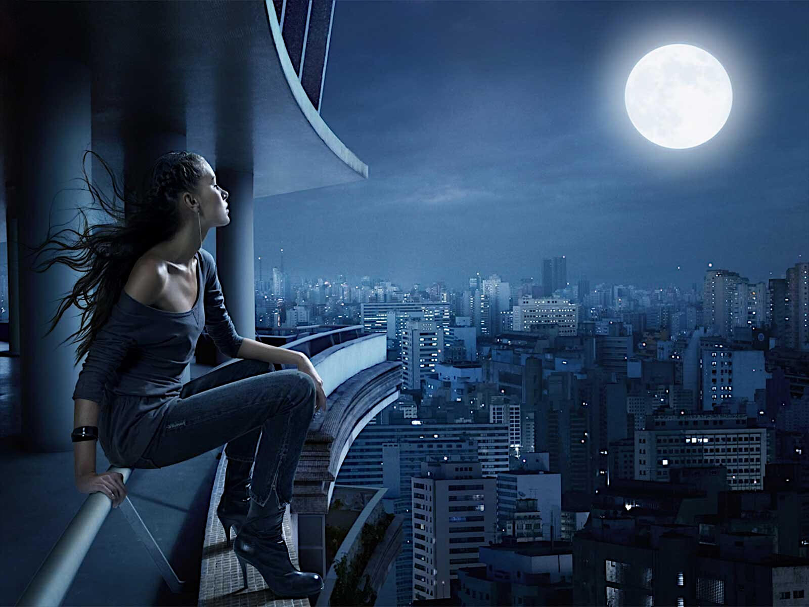 Free photo A girl sits on the edge of a rooftop admiring the city at night.