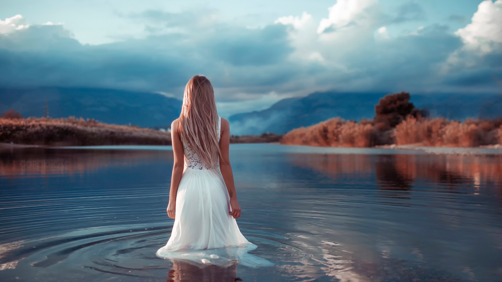 A girl in a light white dress walks into the water