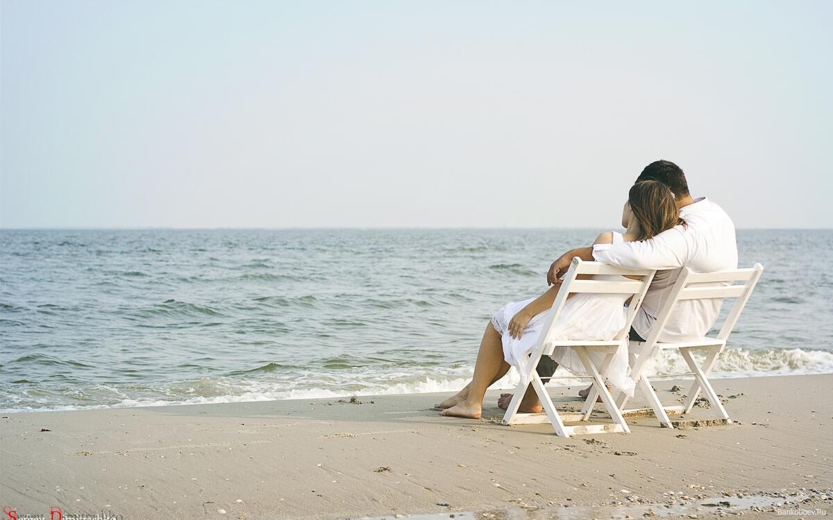 Пара сидит на берегу моря сидит на стульчиках