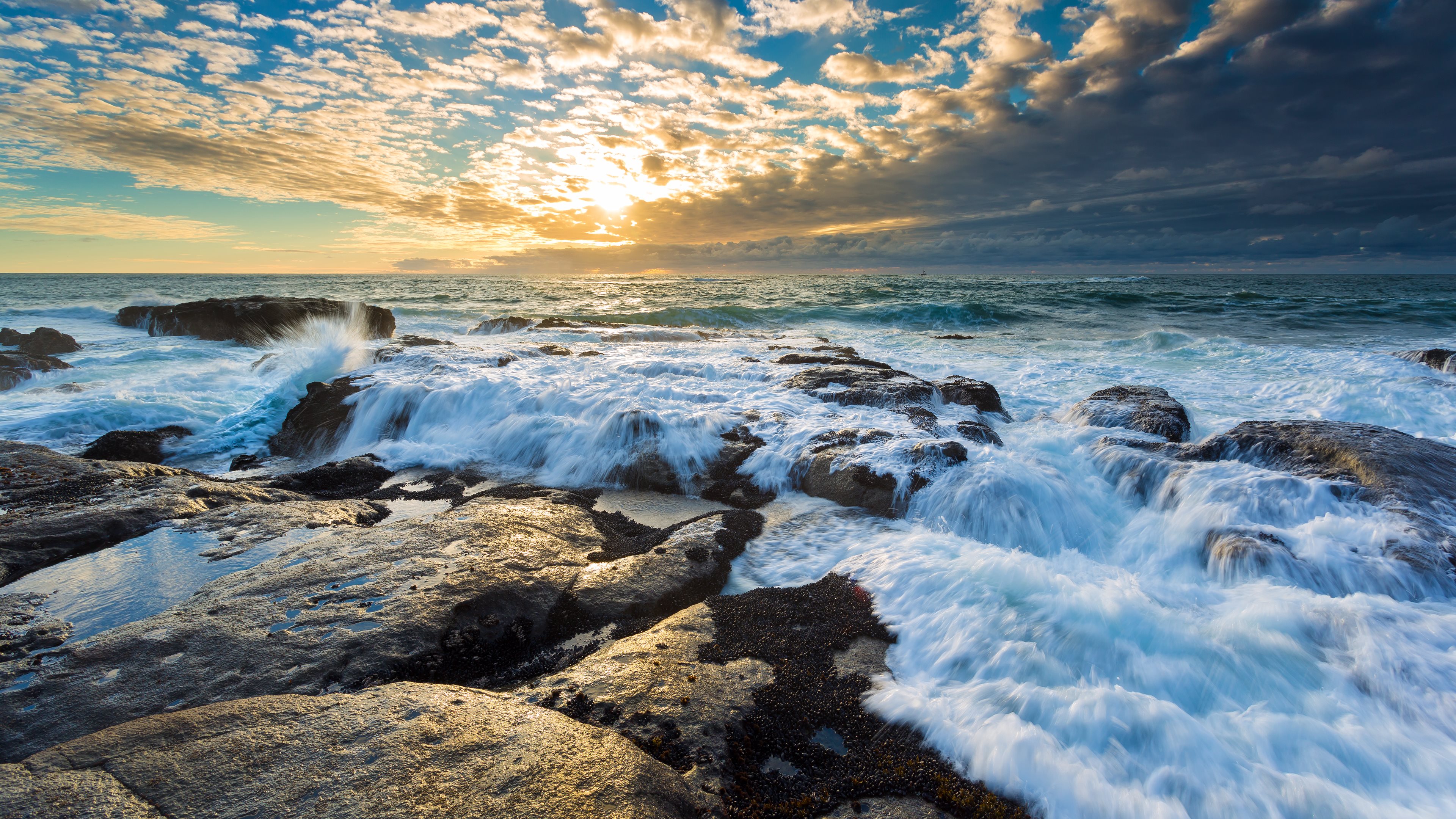 The restless sea beats on the rocks at sunset