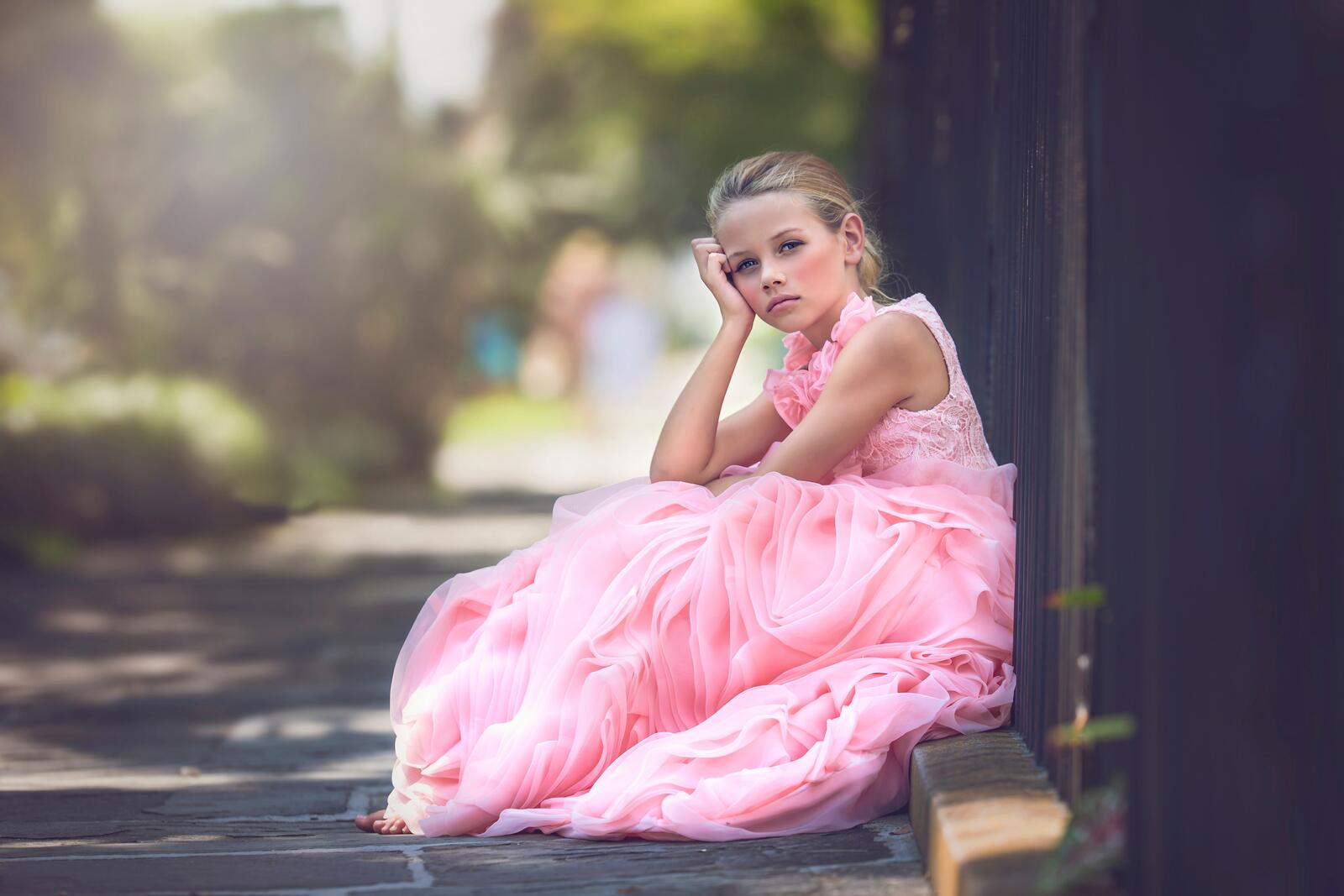 Бесплатное фото Девочка в розовом платье сиди у забора