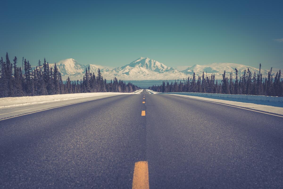 Asphalt road with yellow markings leads to snowy mountains