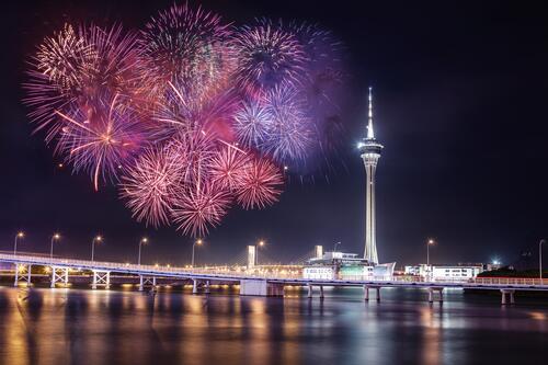 Fireworks next to a tower in a big night city