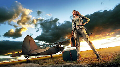 Girl with suitcases standing next to the plane at sunset