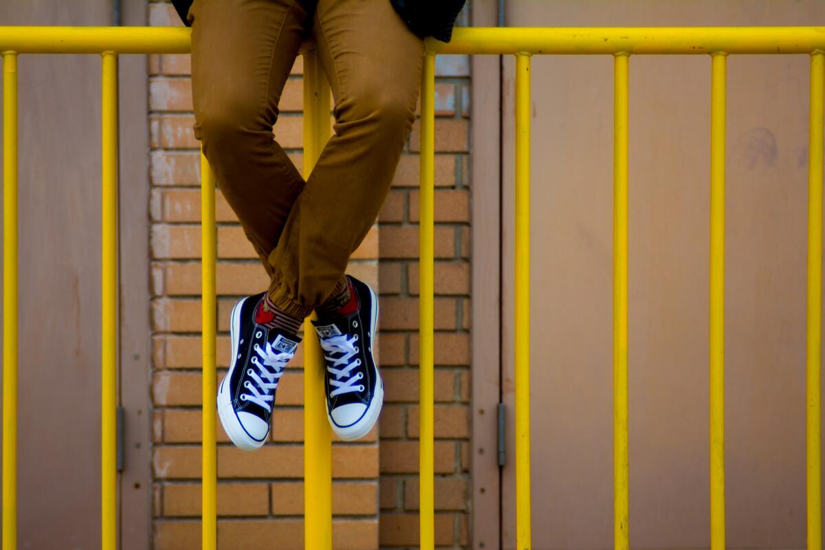 A man in sneakers sits on a yellow fence