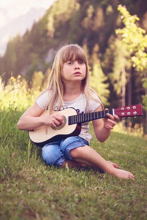 Маленькая девочка с гитарой сидит на зеленой траве
