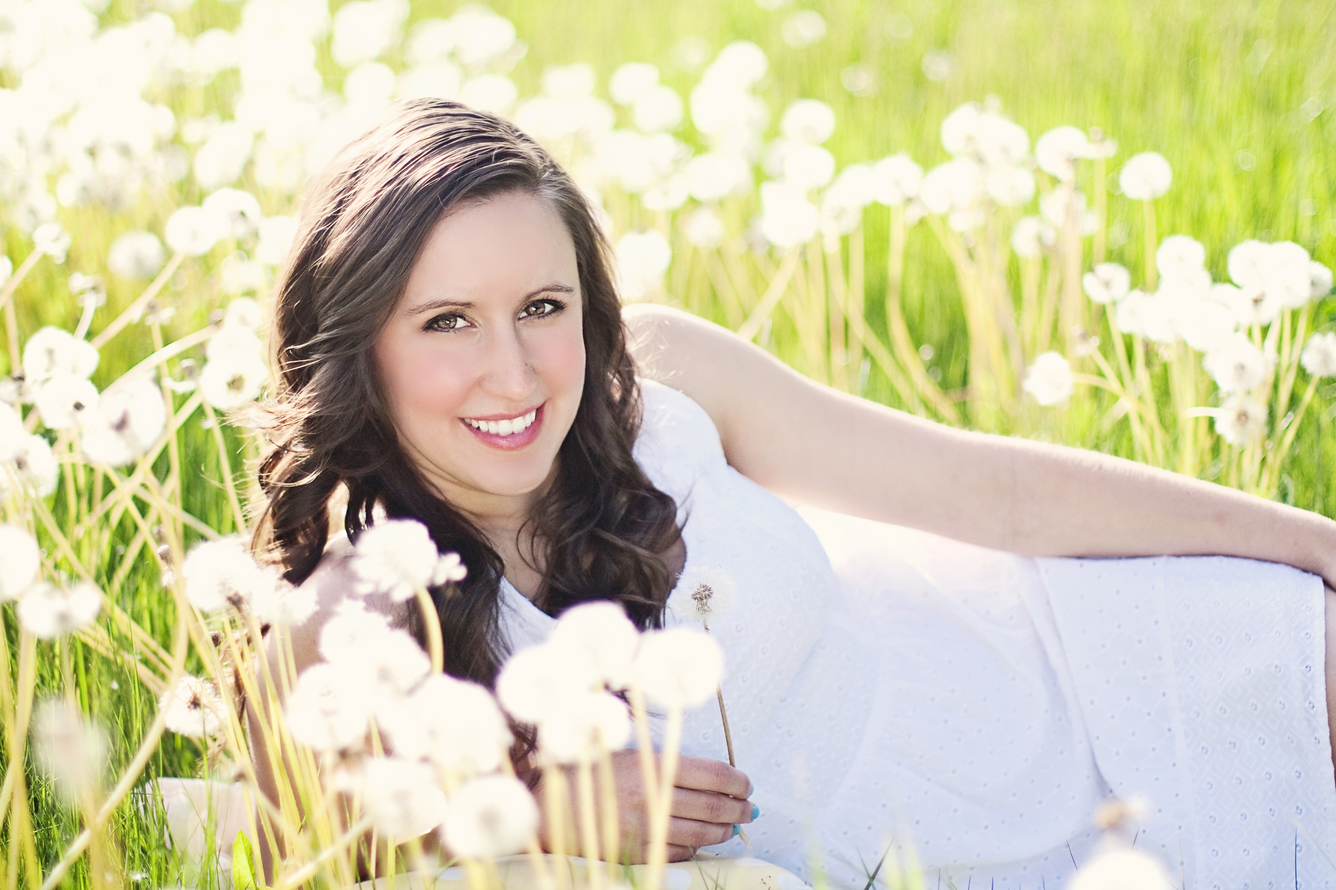 Free photo A dark-haired woman in a white dress lies in a clearing with dandelions
