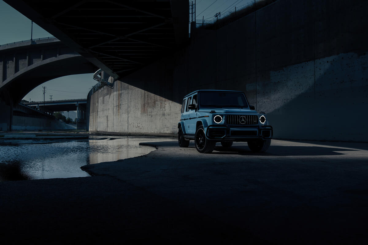 A blue Mercedes G Class stands under the bridge in the evening time