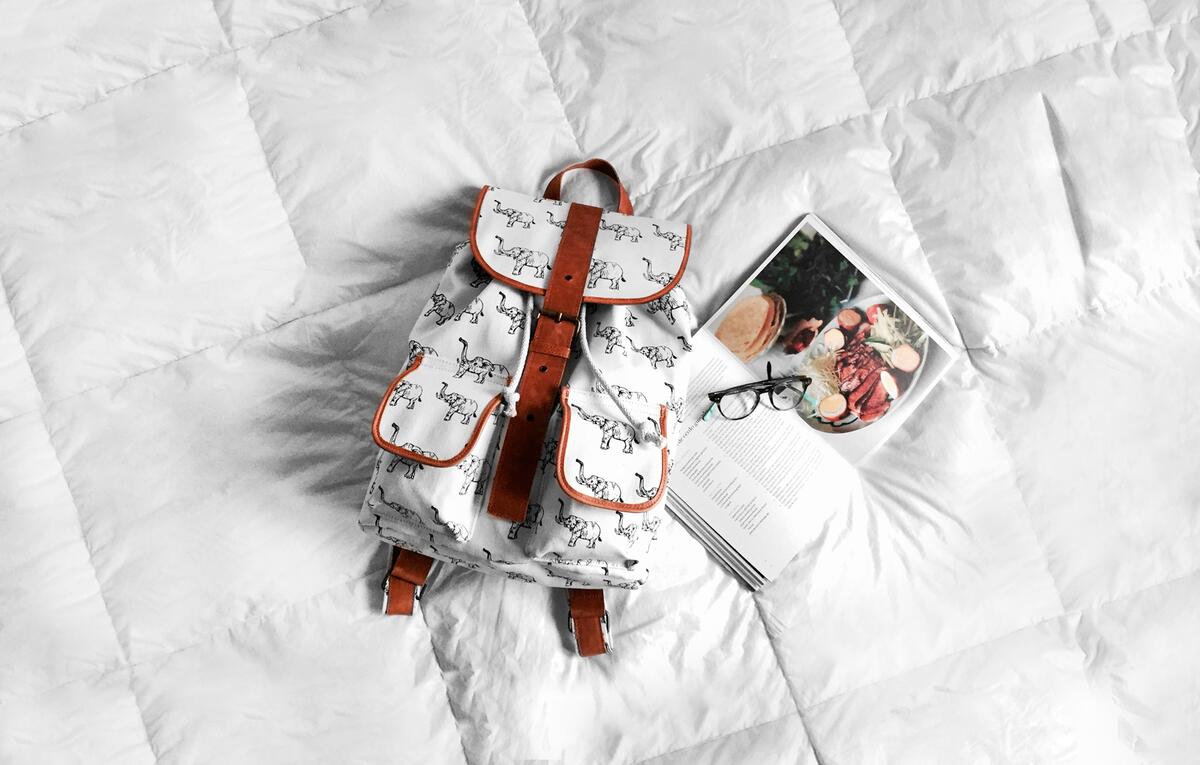 A white backpack lies on a white bed