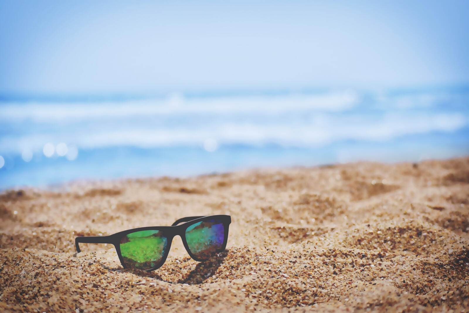 Солнцезащитные очки лежат на песчаном берегу пляжа