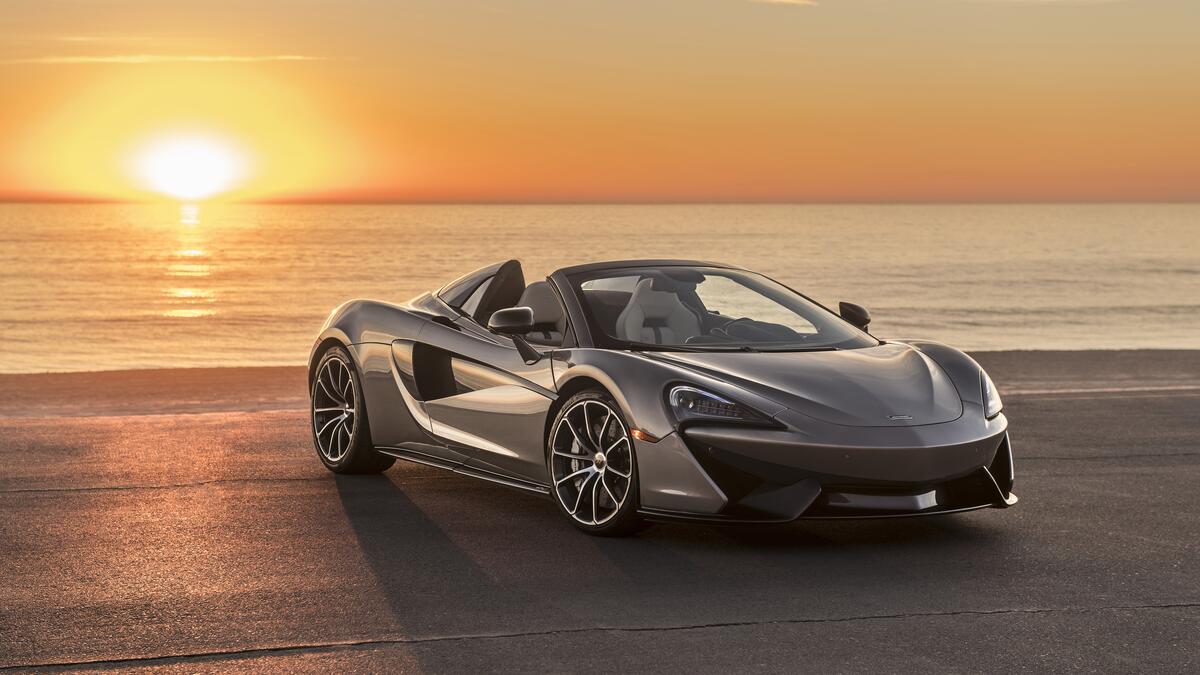 A silver Mclaren 570S Spider convertible on the beach at sunset