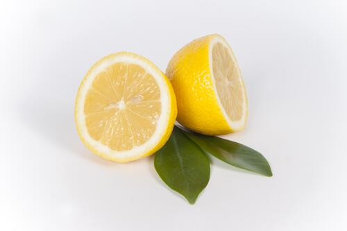 Разрезанный лимон с зелеными листьями на сером фоне