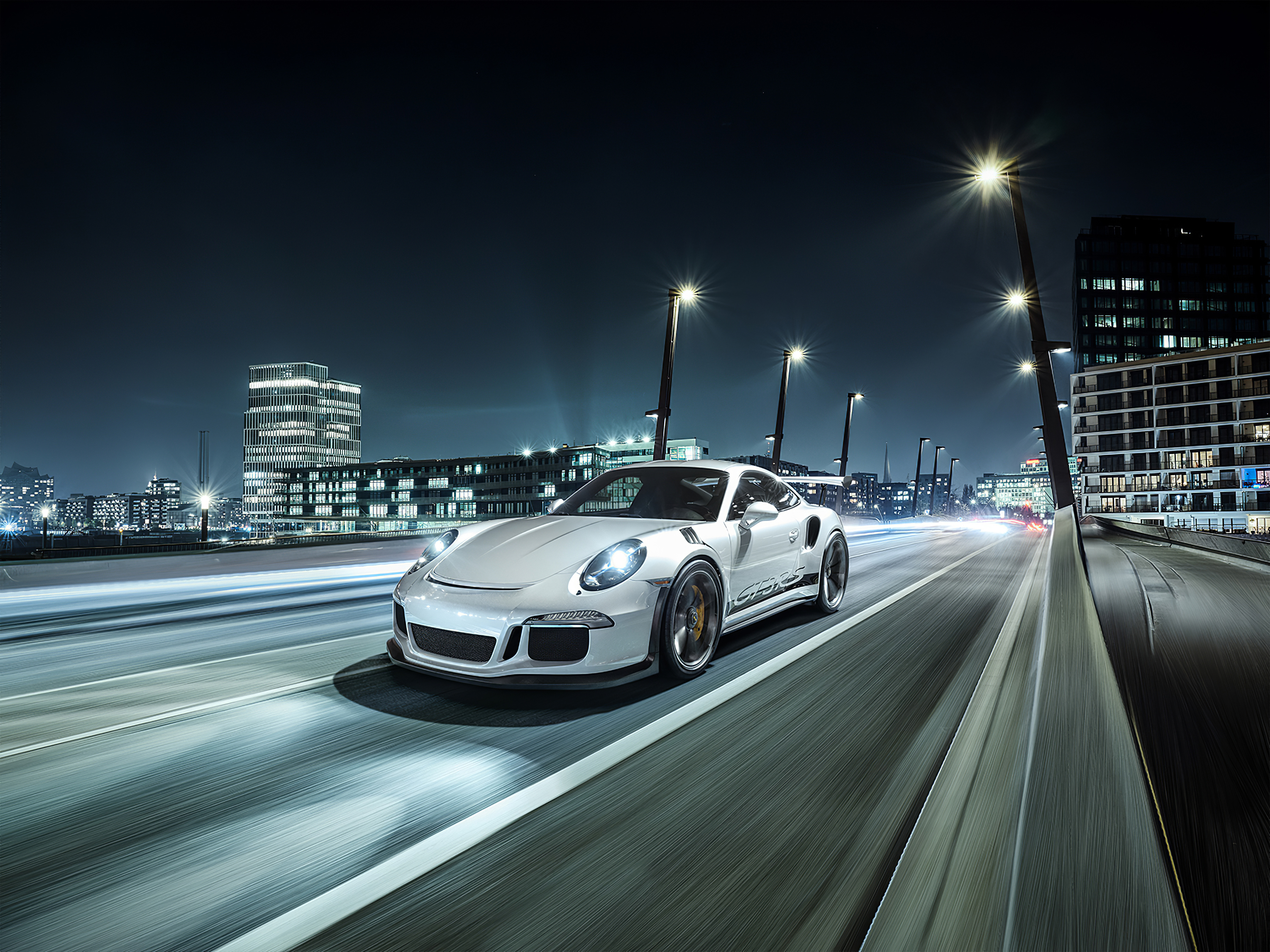 A picture of a white Porsche driving through a city at night.