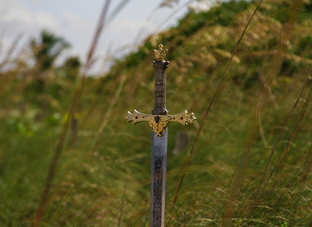 An antique sword with a beautiful hilt is stuck in the ground