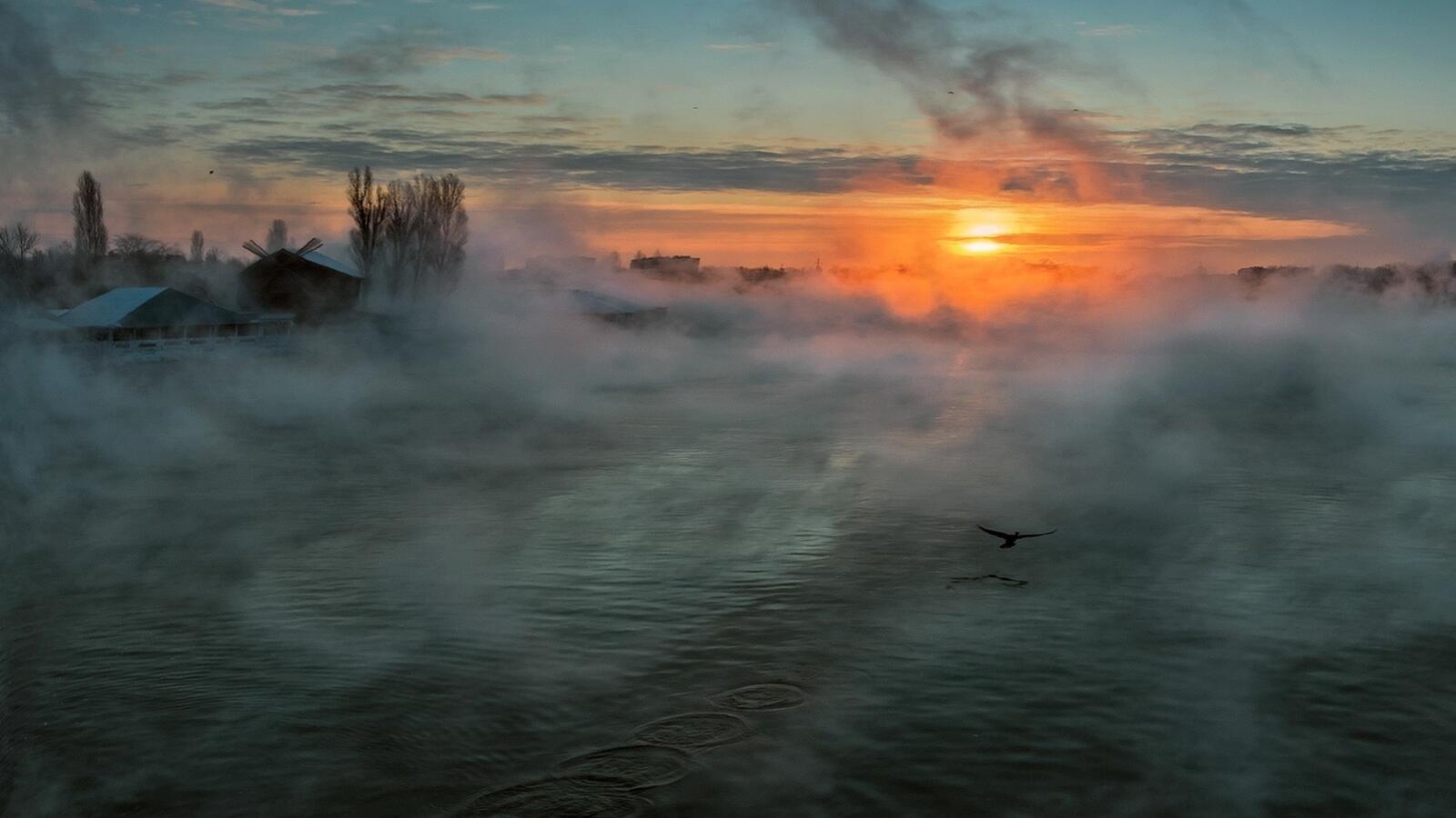 Free photo Smoke billows over the water at sunset.