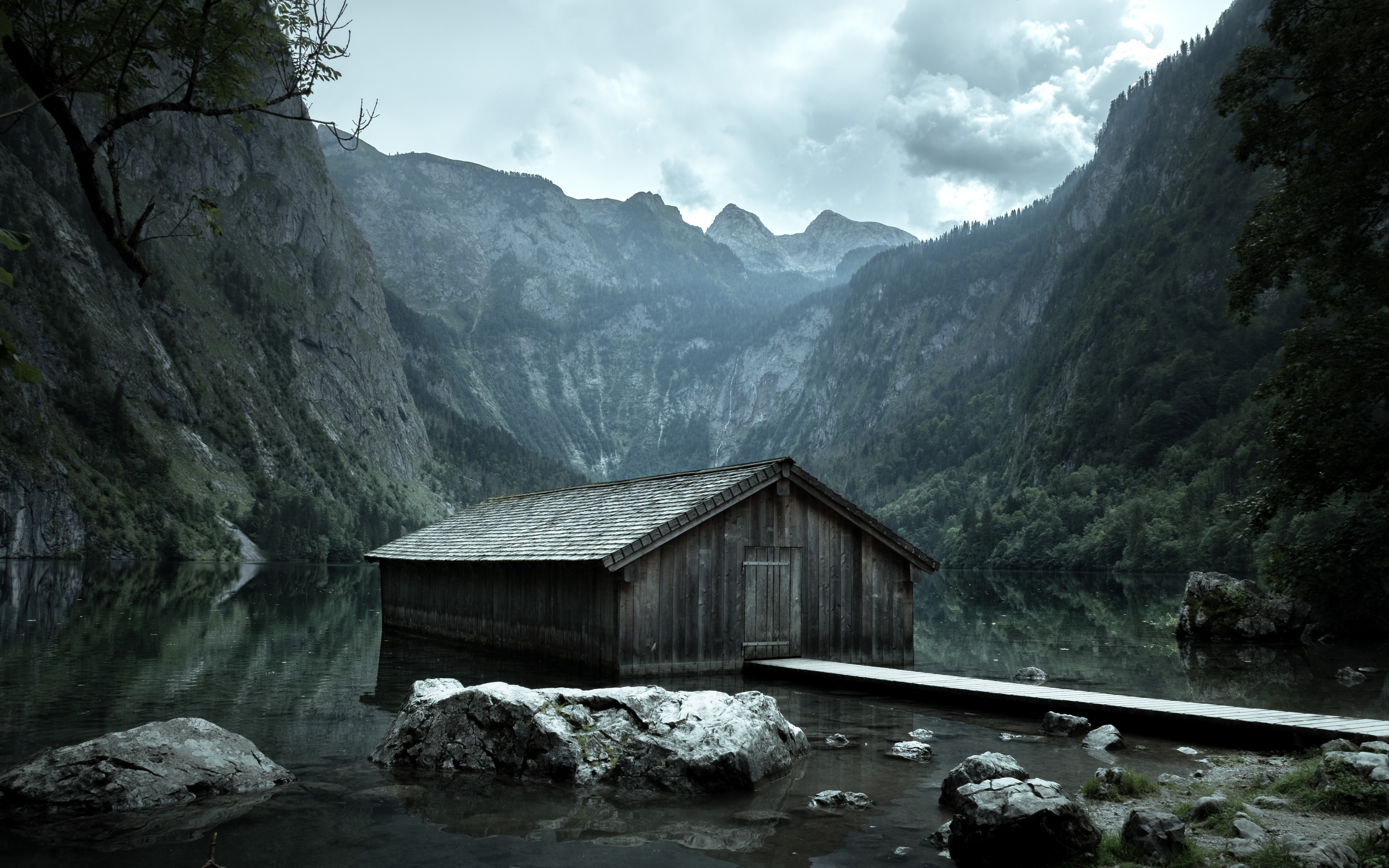 A wooden barn on a lake among the mountains in cloudy weather