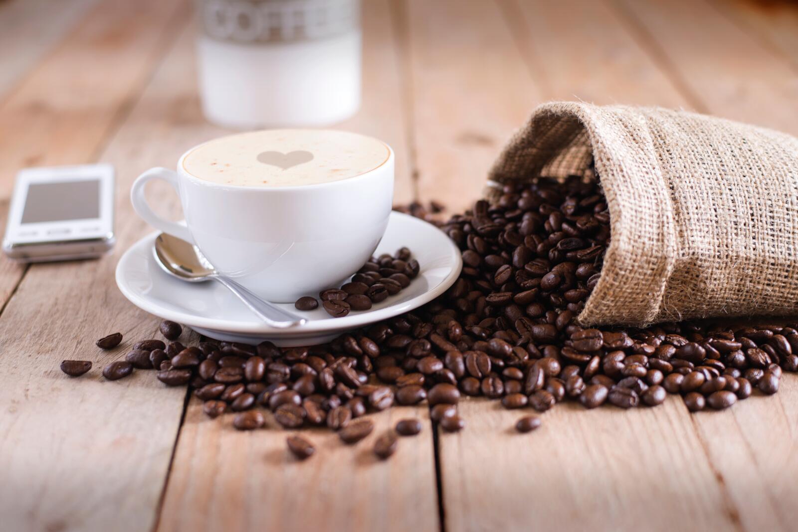 Бесплатное фото Высыпанные кофейные зерна из мешка на чашку с кофе