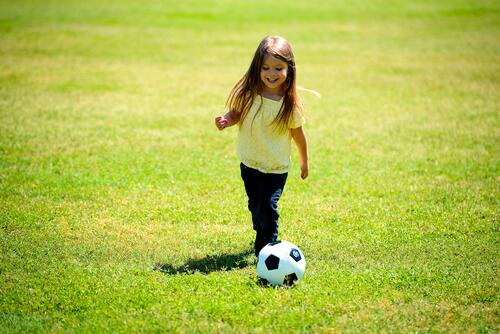 A little girl plays with a soccer ball on a green lawn
