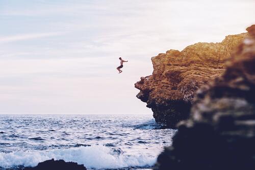 Мужчина прыгает со скалы в море