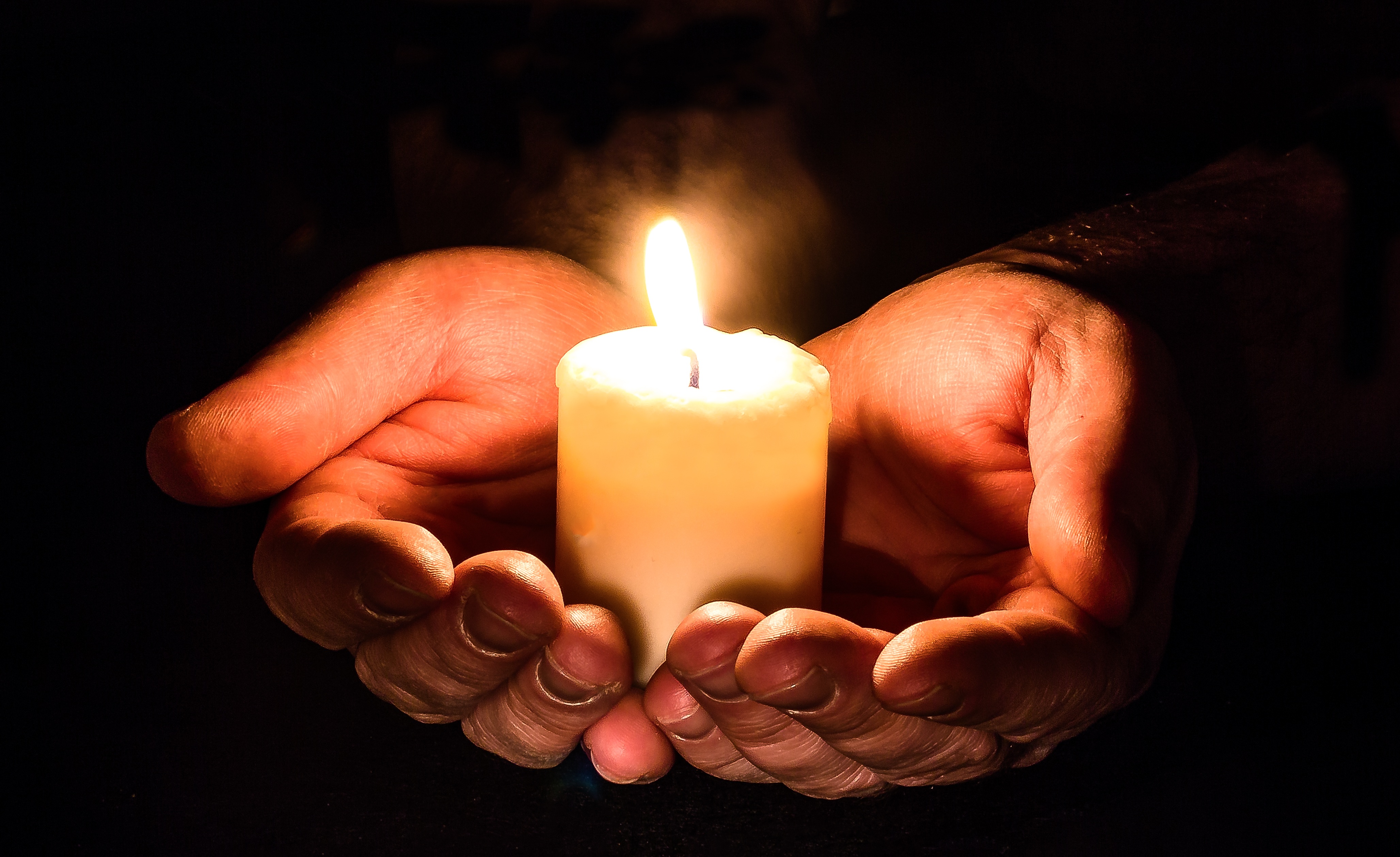 Бесплатное фото Зажжённая свечка в руках на черном фоне